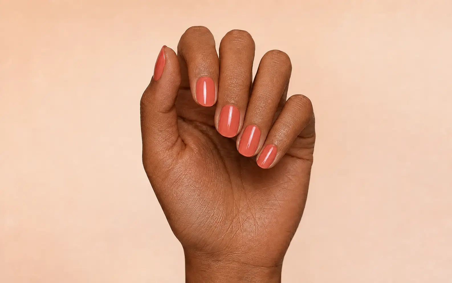 Tan hand wearing Warm Coral professionally rendered polish